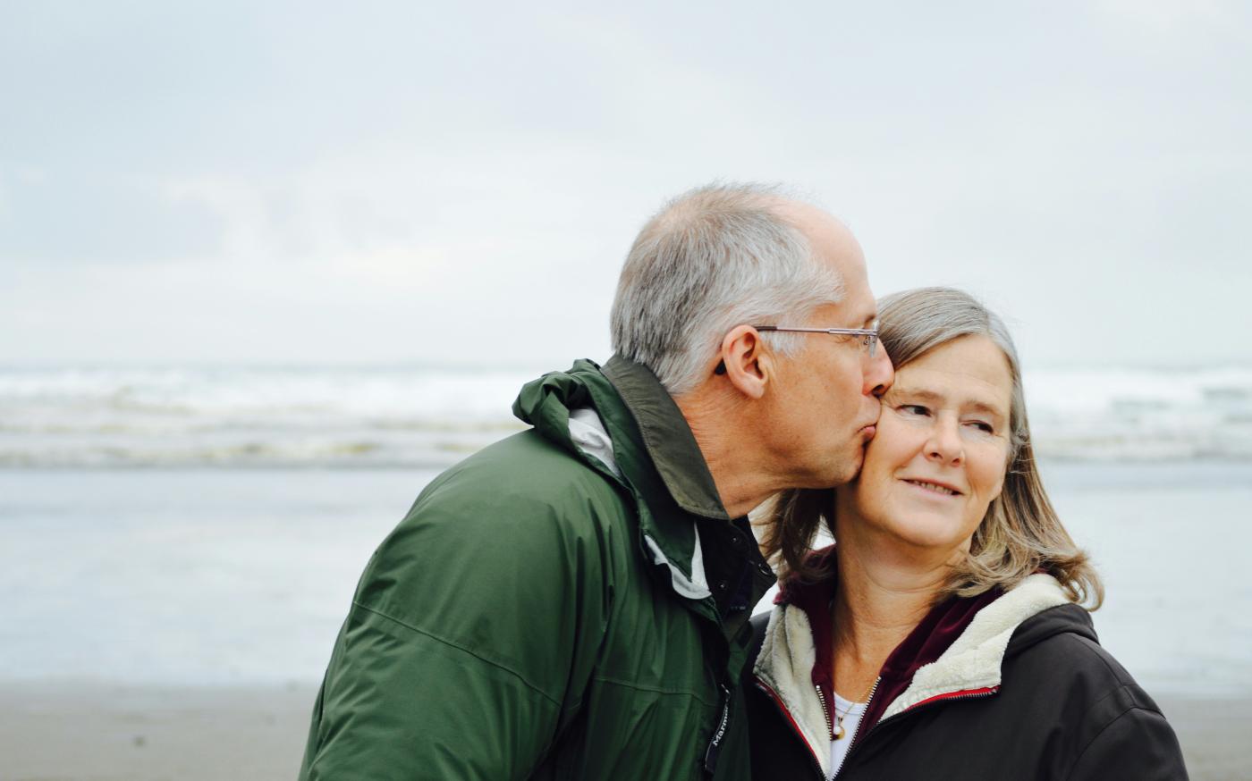 man kissing woman on check beside body of water by Esther Ann courtesy of Unsplash.
