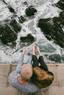 man and woman sitting on cliff near body of water by Justin Groep courtesy of Unsplash.