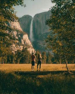 couple standing on tree trunk looking at field and forest by Jared Rice courtesy of Unsplash.