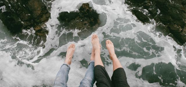 man and woman sitting on cliff near body of water by Justin Groep courtesy of Unsplash.